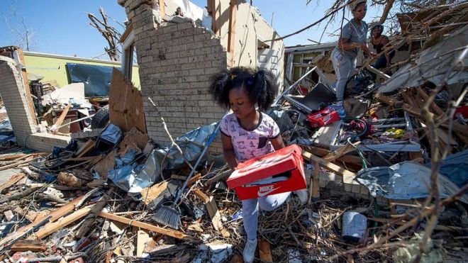 한 소녀가 토네이도가 지나간 잔해에서 물건을 찾고 있다