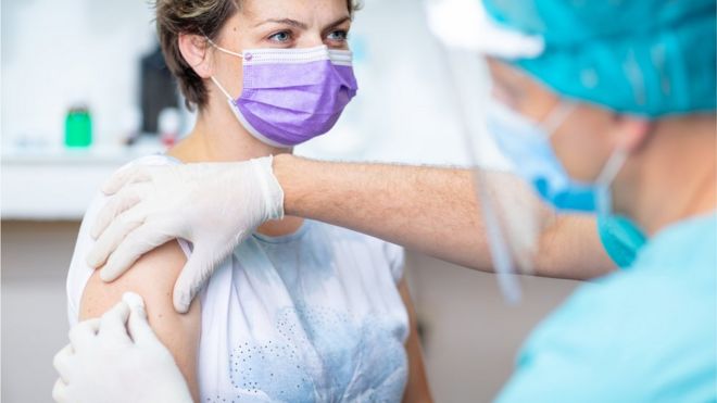 Медсестра в защитном костюме делает пациенту вакцинацию