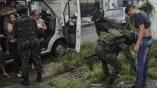 Женщина несет своего ребенка, когда она проходит мимо военной полиции в патруле возле фавелы Вила Кеннеди в Рио-де-Жанейро 23 февраля 2018 года.