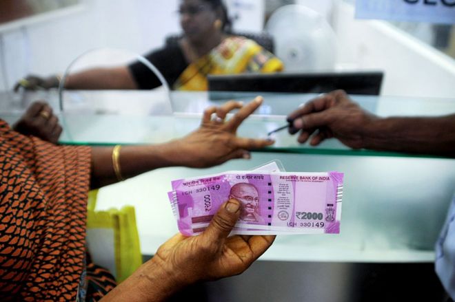На этой фотографии, сделанной 17 ноября 2016 года, индийская женщина держит 2000 банкнот индийских рупий, поскольку на ее пальце отмечены несмываемые чернила после обмена банкнот 500 и 1000 индийских рупий в одном из банков Ченнаи. Правительство Индии признало 31 января, что его решение об изъятии ценных бумаг из обращения вызвало боль во многих секторах экономики, поскольку оно понизило прогноз роста накануне бюджета