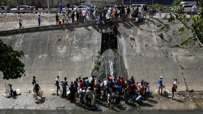 Люди собирают воду из канализационного канала у реки Гвайр в Каракасе 11 марта 2019 года,