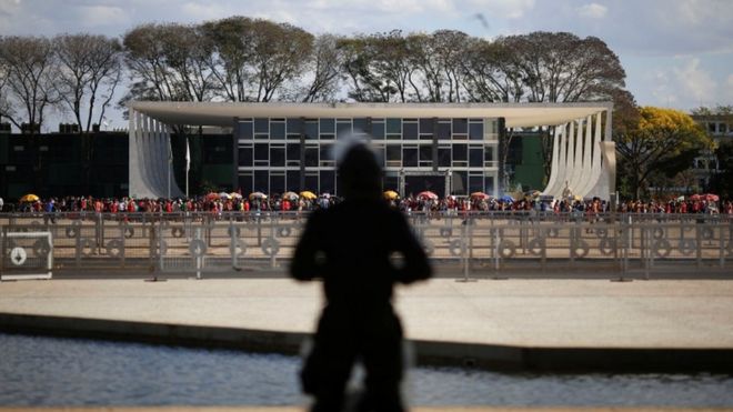 Sombra de guarda em frente a prédio do STF, com vários manifestantes em frente