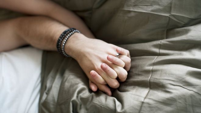 Casal de mãos dadas na cama, em referência a sexo