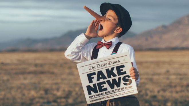 Niño con nariz de Pinocho y sosteniendo una periódico con Fake News.