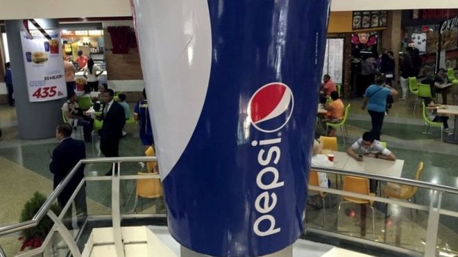 Люди проходят мимо фиктивной гигантской чашки газировки, которая является частью рекламной кампании Pepsi, в торговом центре в Каракасе 20 декабря 2015 года.