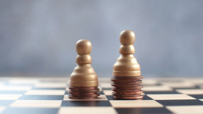 Tabuleiro de xadrez com duas peças apoiadas sobre moedas - uma em uma pilha mais baixa que a outra