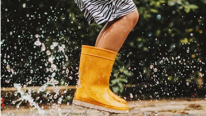 Niño con botas de agua saltando sobre la lluvia.