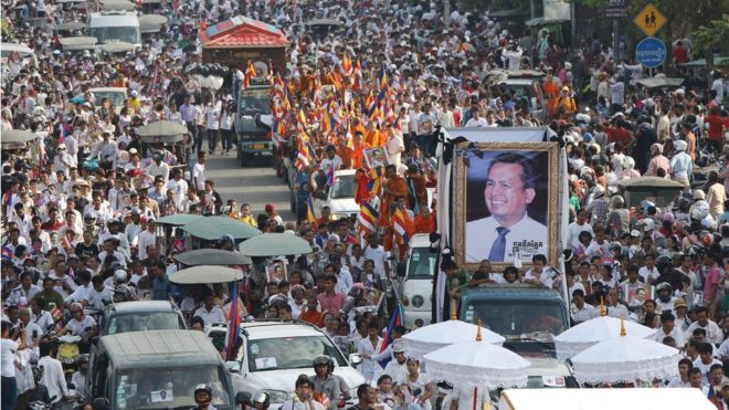 Похоронное шествие для Кема Лея, в том числе большая его фотография, изображающая движение по улицам Пномпеня