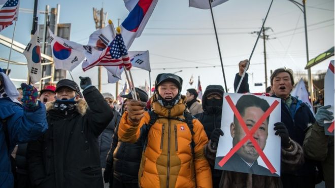 Протестующие держат американские и южнокорейские флаги и вычеркнута вывеска с лицом Ким Чен Ына.