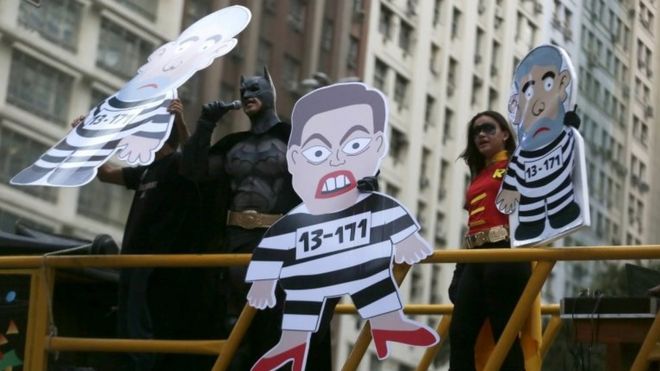 Демонстрант в костюме Бэтмена выступает рядом с картонными вырезами с изображением Дилмы Руссефф и бывшего президента Луиса Инасиу Лула да Силвы во время акции протеста в Рио-де-Жанейро 3 сентября 2015 года