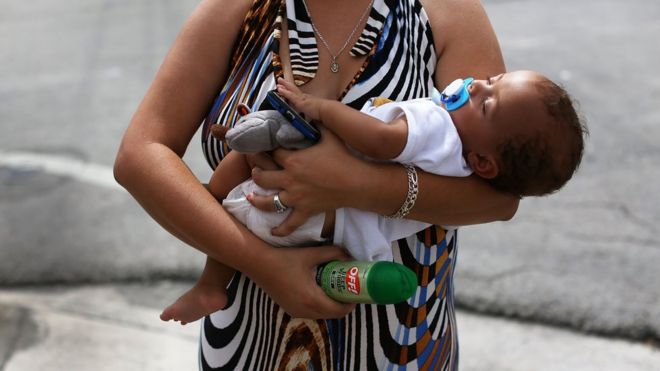 Женщина держит своего ребенка после того, как ей дали баллончик со средством от насекомых в Майами, Флорида