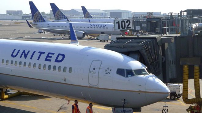 Two ground crew members walk past a United Airlines airplane as it sits at a gate at Newark Liberty International Airport