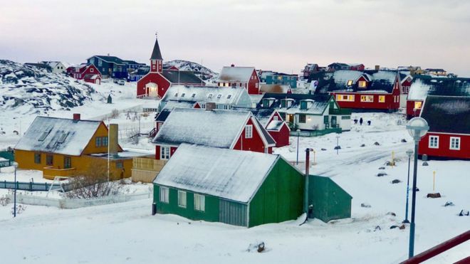 Изображен город в типичном гренландском стиле - ярко окрашенные деревянные стены и треугольные крыши, покрытые снегом, являются основными чертами этих домов с редкими точками