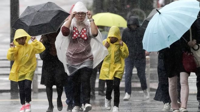 Pedestres têm dificuldade para caminhar por causa de chuva e vento fortes