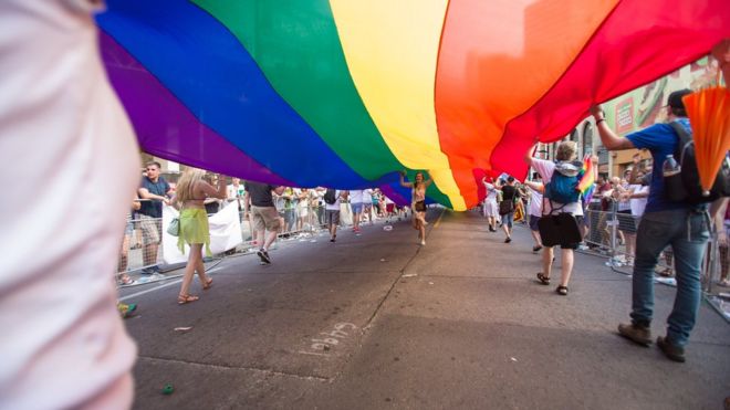 Женщина бежит под гигантским радужным флагом во время парада WorldPride 2014 в Торонто, Канада, 29 июня 2014 года.