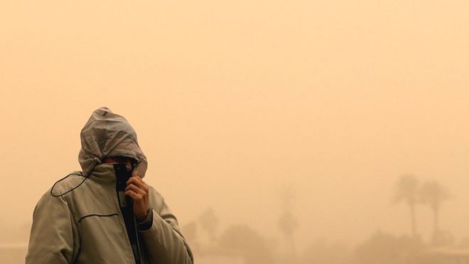 Um homem cobre o rosto com a jaqueta para evitar inalar o pó da tempestade de areia do Cairo