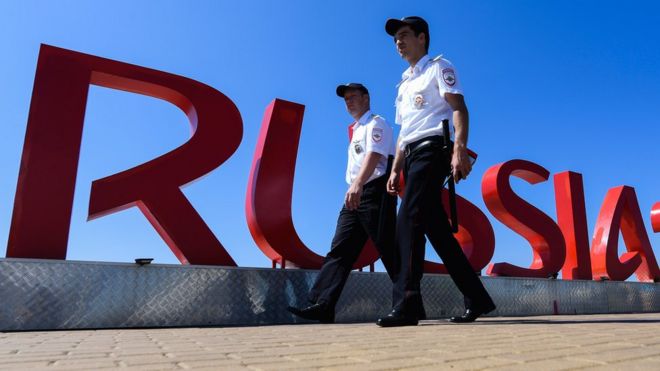 Security personnel walk past a Russia 2018 sign near the Fisht Olympic Stadium in Sochi on June 12, 2018