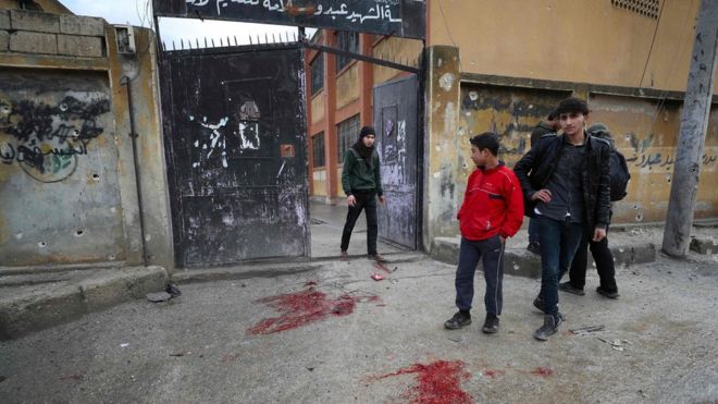 People stand next to patches of blood outside a school in the opposition-held town of Sarmin, Syria, that was reportedly hit by cluster munitions fired by government forces (1 January 2020)