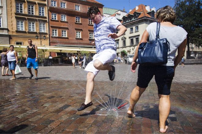Люди охлаждают себя спринклерами во время жары в Варшаве