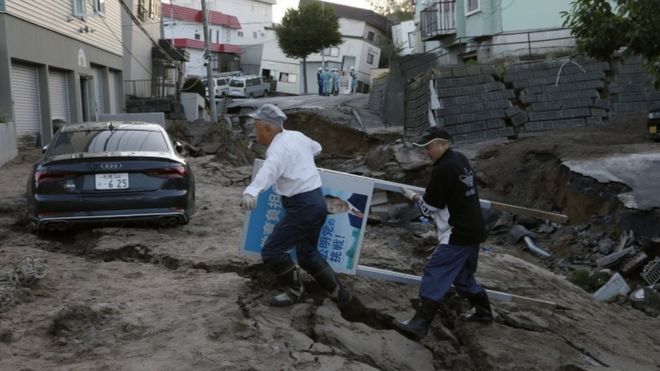 Imagem mostra uma das ruas afetadas pelo terremoto na provÃ­ncia de Hokkaido, no Japão, onde dois homens carregam placa de polÃ­tico