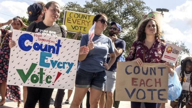 Толпа протестующих требует пересчета голосов у здания избирательного департамента Майами-Дейд во Флориде, 10 ноября 2018 года