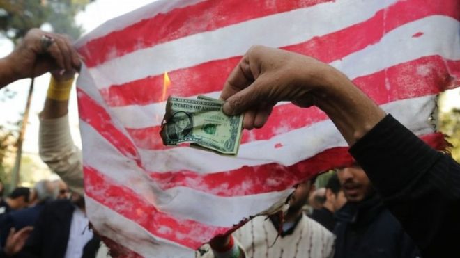 An Iranian protester burns a US banknote