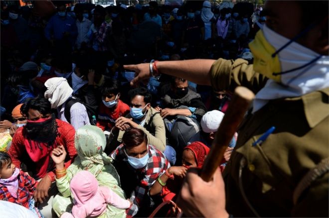 A police officer instructs migrant workers and their family members to line-up as they leave India's capital for their homes during a government-imposed nationwide lockdown as a preventive measure against the COVID-19 coronavirus