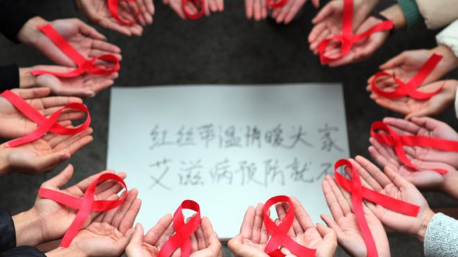 This picture taken on 30 November 2015 shows volunteers holding red ribbons above a piece of paper written in Chinese that reads ''Red ribbons bring warmth to everyone to prevent AIDS' during an event for World Aids Day in Chongqing