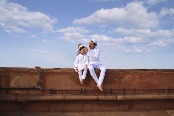 A father and son sitting in white traditional attire with blue sky behind