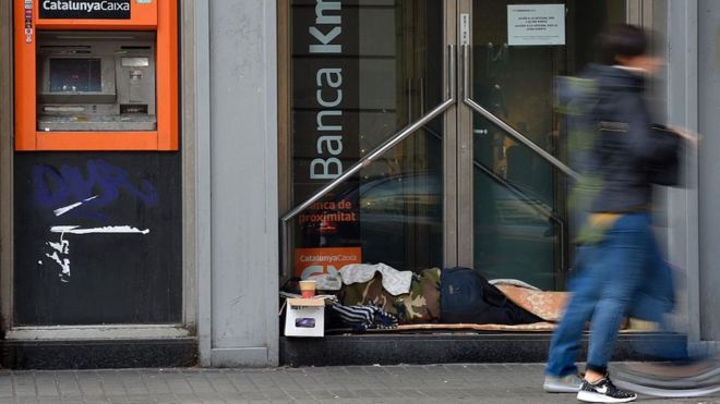 Una persona sin hogar descansa en la puerta de un banco de Barcelona