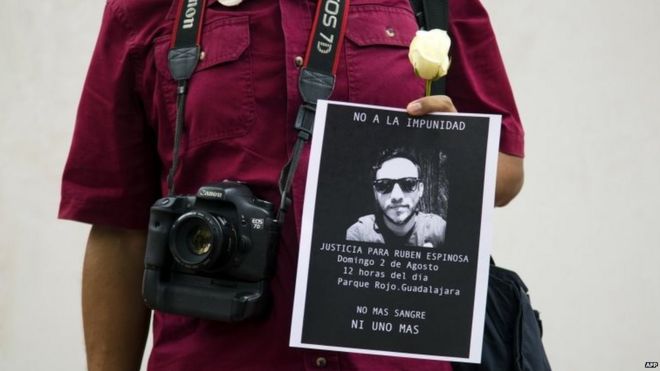 Фотожурналист держит белый цветок и фотографию убитого фотожурналиста Рубена Эспиноса во время демонстрации 2 августа 2015 года
