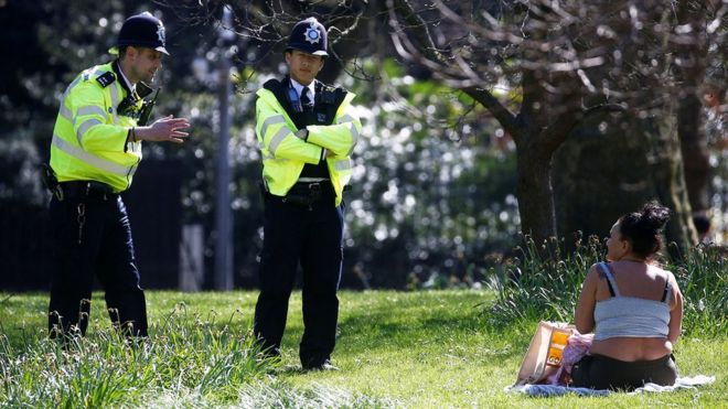 Police speak to a woman sunbathing in a park