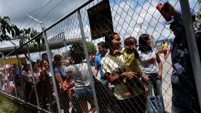 Pessoas formam fila atrás de grade em Paracaraima, na fronteira entre Brasil e Venezuela