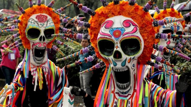 Люди в гигантских масках черепа и много цветов и украшений