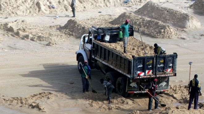 Мужчины грузят грузовик с морским песком на пляже в Сенегале