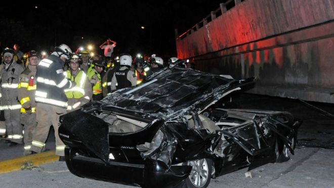 Rescue workers examine a destroyed car after the collapse of a bridge in Guayaquil, Ecuador