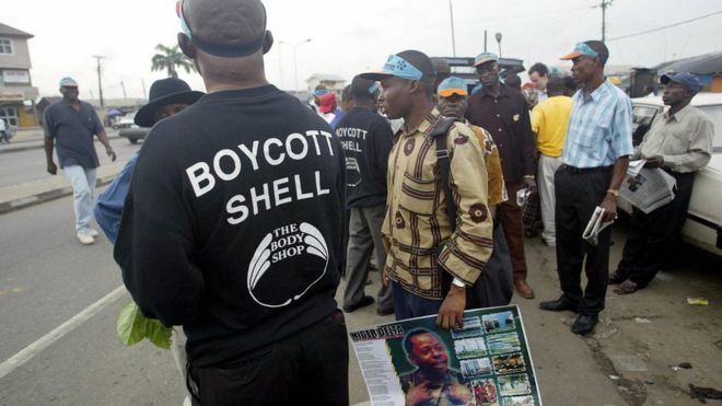Мужчина в футболке в защиту бойкота масла Shell стоит рядом с другим, несущим плакат с изображением Кена Саро-Вива во время митинга на шоссе Порт-Харкорт 10 ноября 2005 г.