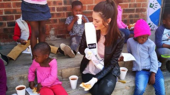 Miss South Africa wearing gloves with food around Soweto orphans
