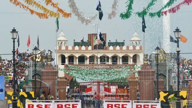 A Pakistani Ranger (top) unfurls the Pakistani national flag as Pakistani people (R/L) watch during a ceremony to celebrate Pakistan's Independence Day at the India-Pakistan Wagah border post on 14 August 2017