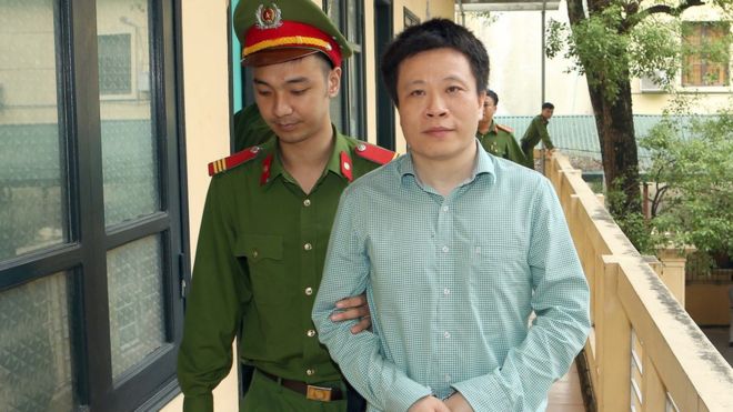 Изображение показывает, что Ха Ван Тхама ведут в суд