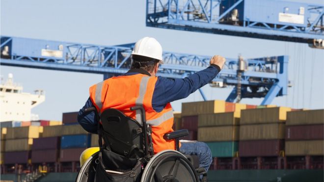 Инженер по транспорту в инвалидной коляске дает указания по отгрузке контейнеров в порту отгрузки