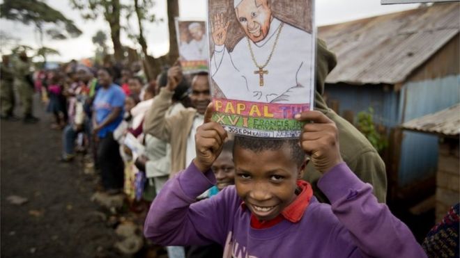 Мальчик держит фотографию папы Франциска, ожидающего его прибытия в католическую церковь Святого Иосифа Рабочего в трущобах Кангеми в Найроби, Кения