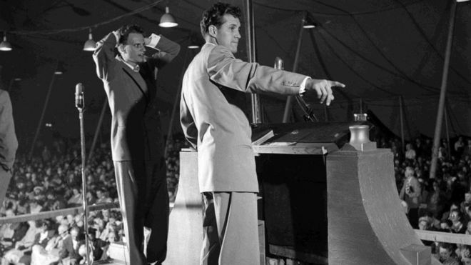 Билли Грэм (слева) стоит с музыкальным руководителем Клиффом Барроусом на кафедре в палатке возрождения, Лос-Анджелес, Калифорния, 21 ноября 1949 г.