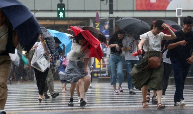Пешеходы, пересекающие дорогу, борются с сильным ветром и дождем в Токио, Япония, 28 июля 2018 года