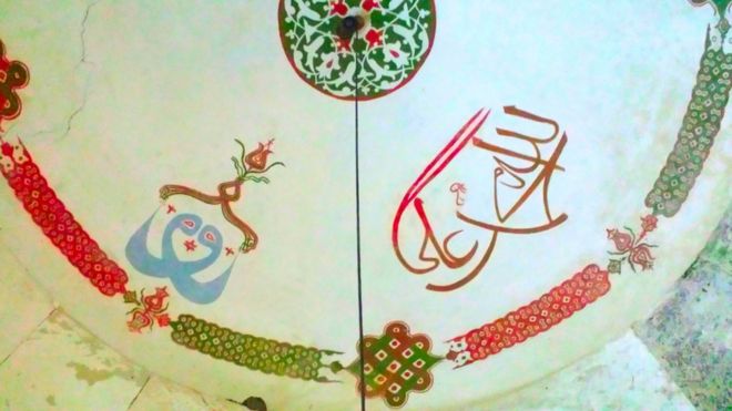 Надписи на потолке Демир Баба Текке, мавзолей Алеви в северо-восточной Болгарии. На правой стороне имена Аллаха, Мухаммеда и Али написаны разборчивым, простым арабским языком. Левая сторона показывает синий мистический образец, в котором все три имени были связаны.