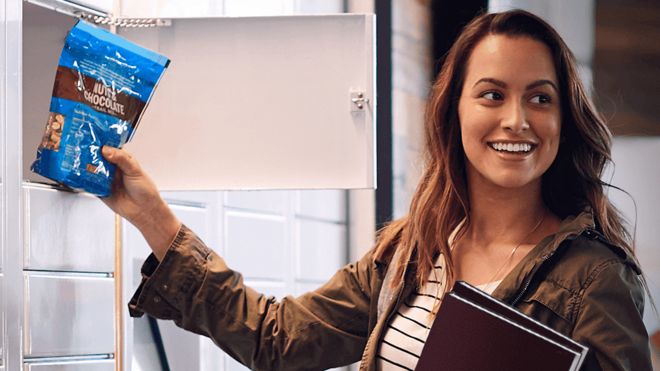 Woman takes a packet of nuts and chocolates out of an Amazon self-service locker