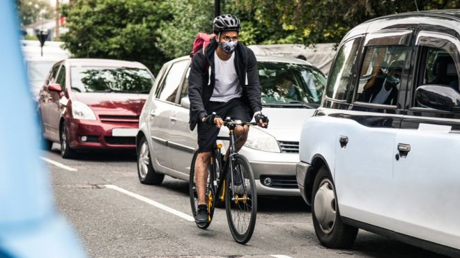 Велосипедист пригородных поездок через центральное лондонское движение во время ношения маски загрязнения.