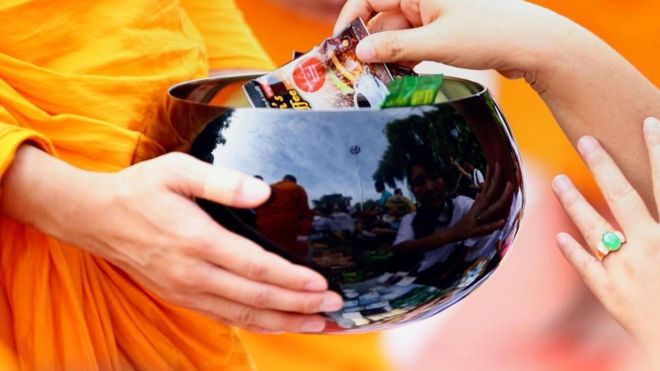 Una persona poniendo dinero en un bol de un monje