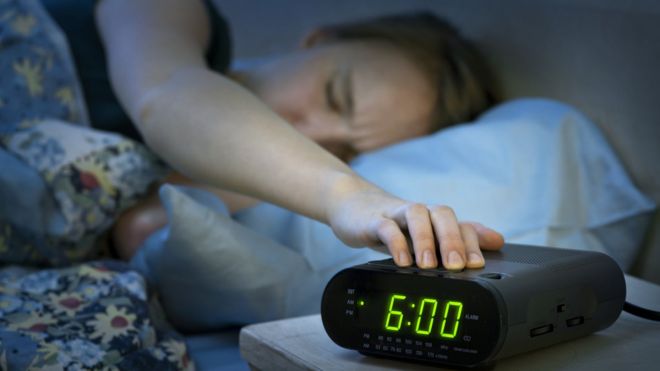 tired woman reaching for alarm clock