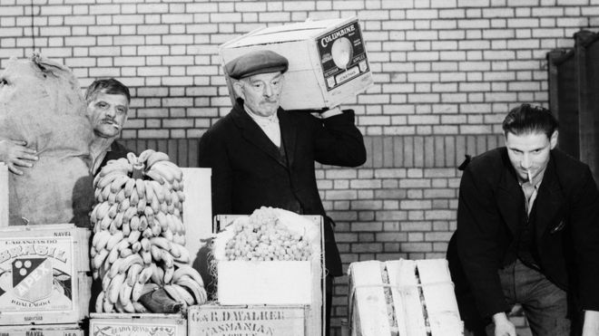 Трое мужчин с коллекцией фруктов и овощей на старом рынке Спиталфилдс, готовые к отправке в лагерь беженцев для испанских детей в Стоунхеме, графство Хэмпшир,